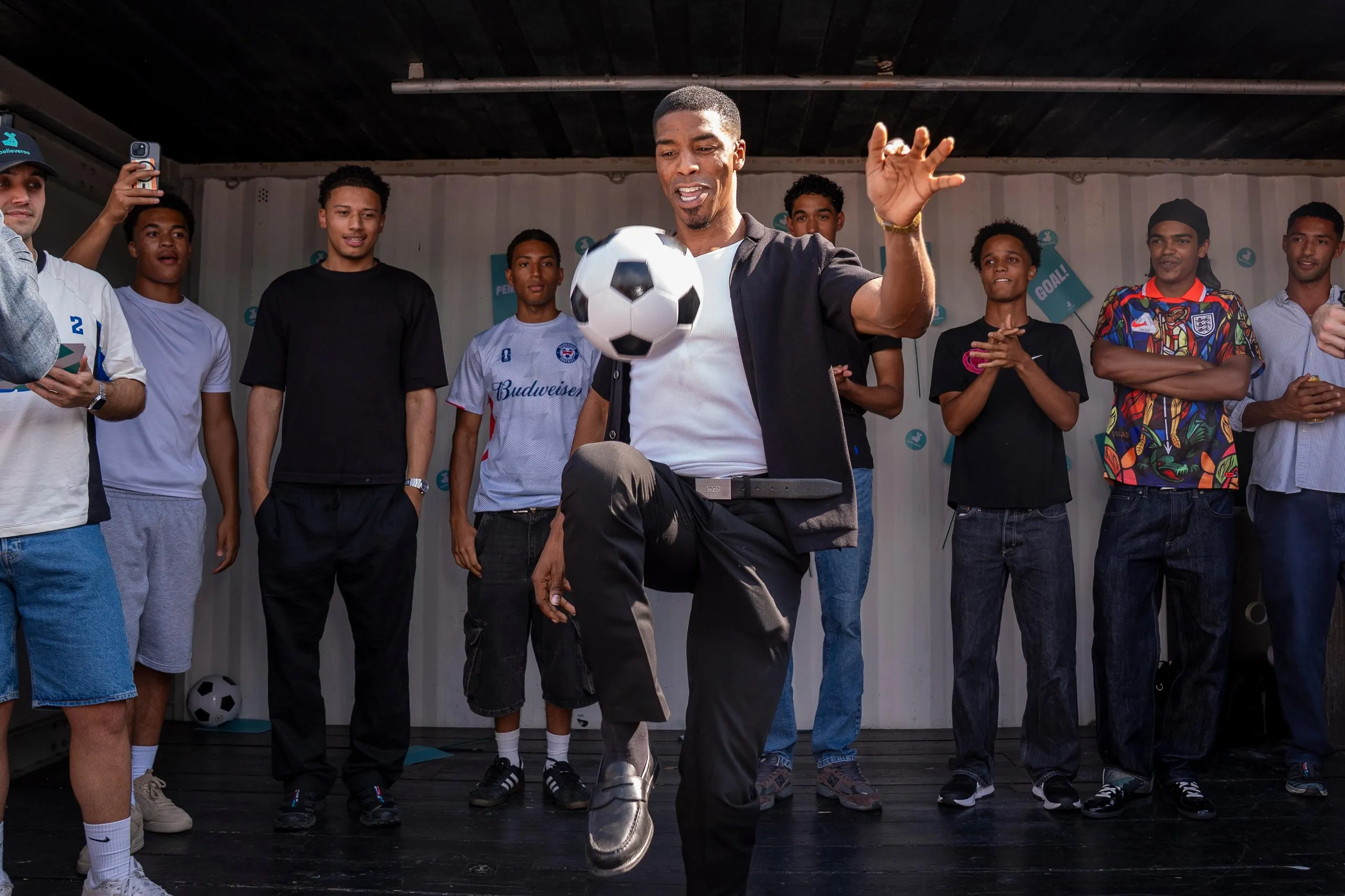 Participants in the Jude Bellingham lookalike competition stand onstage at Boxpark. In the foreground, one contestant is showing off his keepy-uppy skills. 